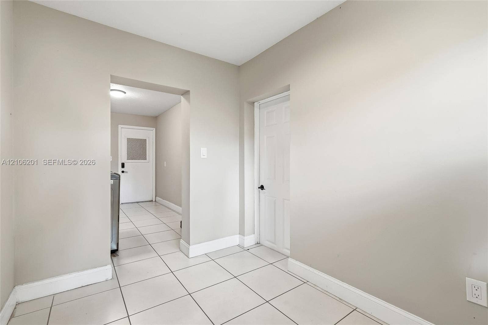 Neutral-toned interior space featuring ceramic tile flooring, a six-panel interior door with matte black hardware, and an exterior door with a glass inlay panel
