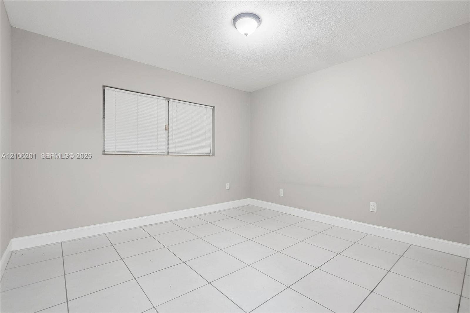 Neutral-toned interior room featuring large-format ceramic tile flooring, a dual-pane horizontal sliding window, and a ceiling-mounted flush light fixture