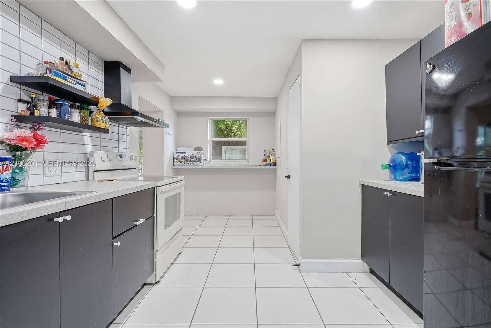Kitchen featuring matte dark cabinetry, white tiled backsplash, light-toned countertops, recessed lighting, and tile flooring