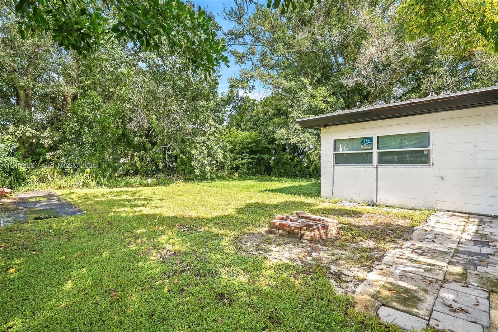 Spacious backyard featuring a brick fire pit, stone paver pathway, and mature tree canopy