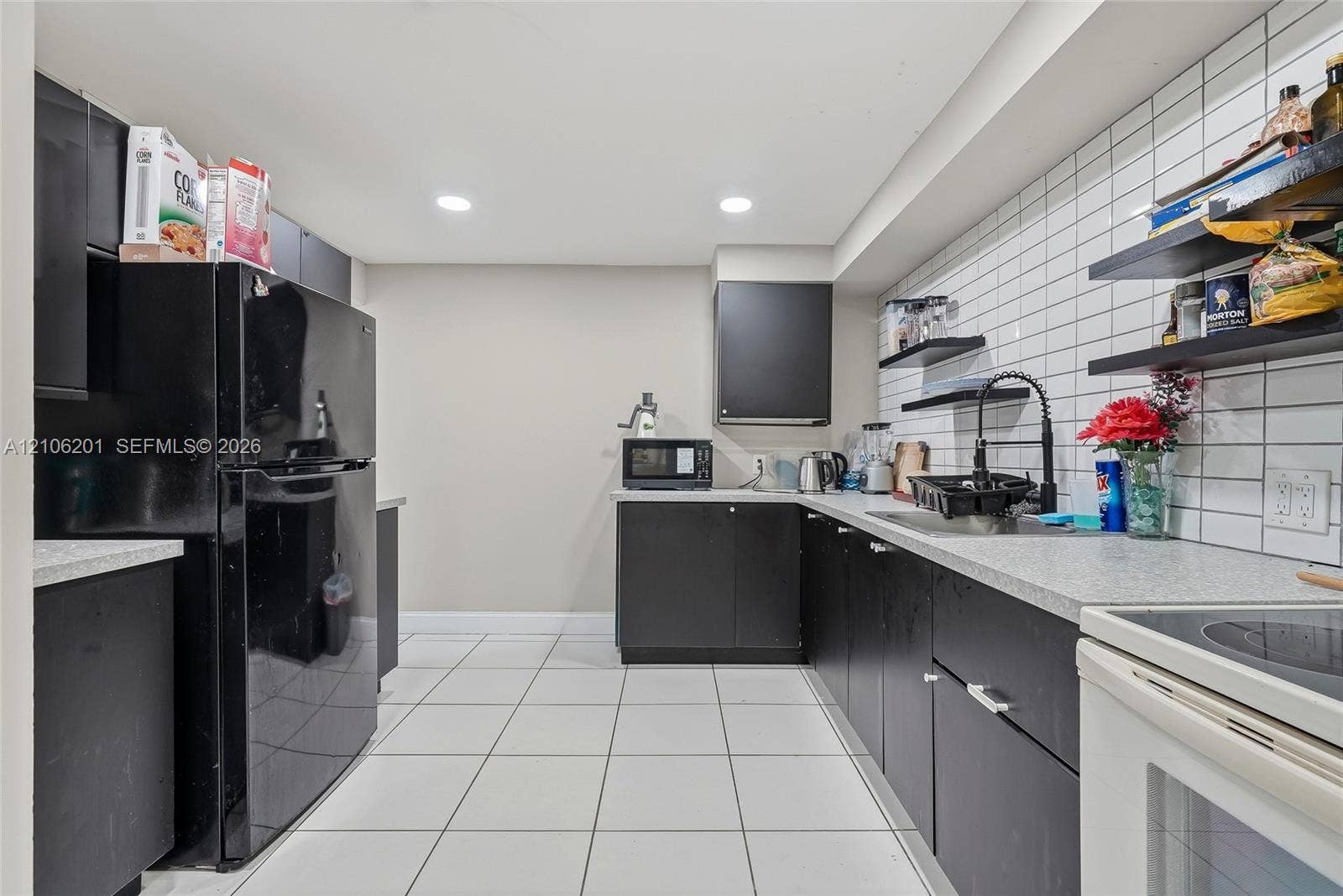 Kitchen featuring matte black flat-panel cabinetry, light-toned countertops, white subway tile backsplash, recessed ceiling lighting, and tile flooring