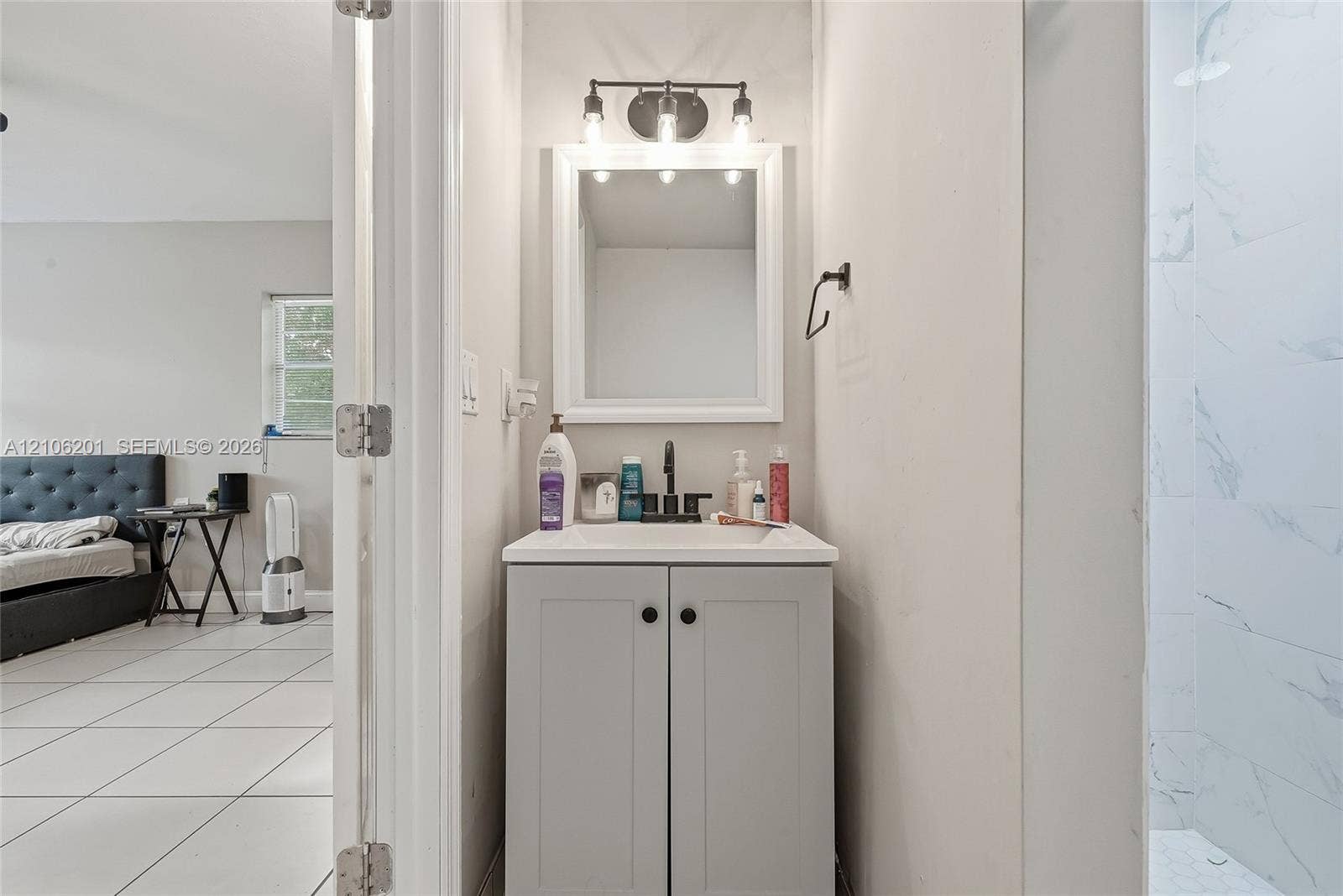Light grey Shaker-style vanity with a rectangular sink, matte black faucet, framed mirror, and three-bulb vanity light fixture