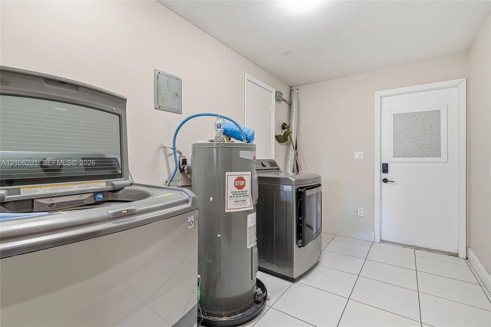 Utility room featuring large-format ceramic tile flooring, a dedicated water heater, and an exterior door with a decorative glass panel