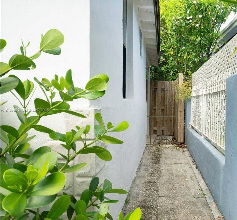 2121 SW 13th Avenue, #Studio, Miami, Miami, FL 33145 Exterior side path featuring white stucco wall, concrete walkway, decorative lattice fencing, and wooden privacy gate