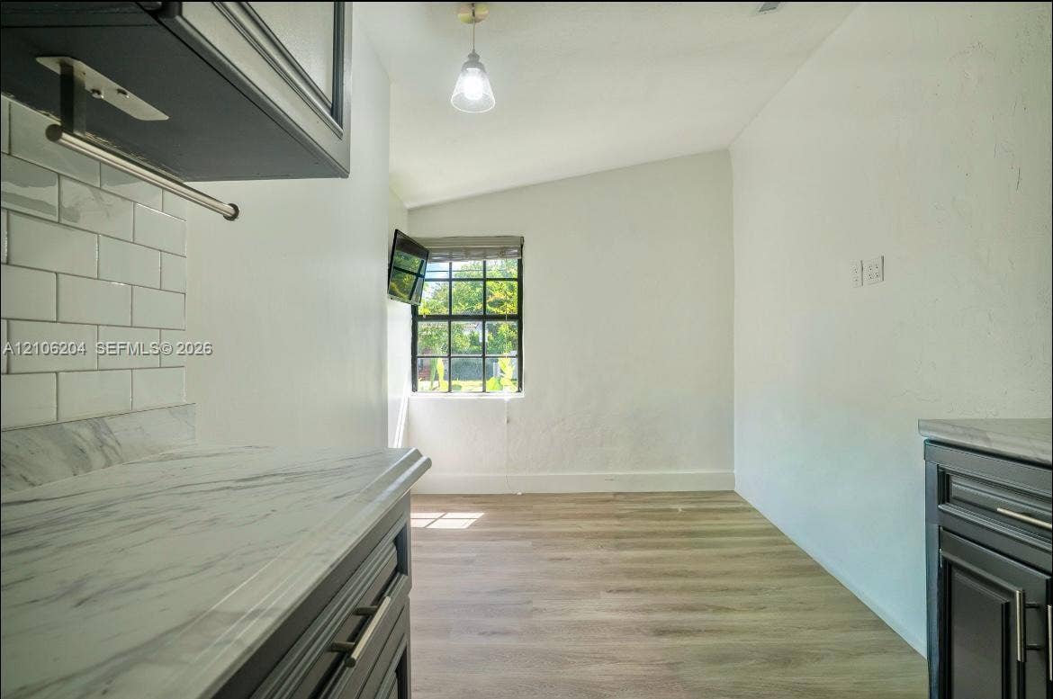 2121 SW 13th Avenue, #Studio, Miami, Miami, FL 33145 Kitchen featuring dark cabinetry, stone-finish countertops, white subway tile backsplash, wood-finish flooring, and a multi-pane window