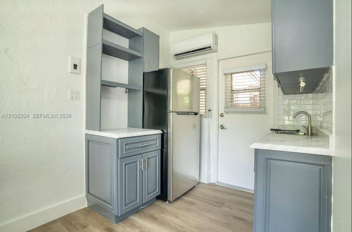 2121 SW 13th Avenue, #Studio, Miami, Miami, FL 33145 Kitchen featuring gray shaker-style cabinetry, white countertops, light-toned wood-finish flooring, stainless steel refrigerator, and wall-mounted climate control unit