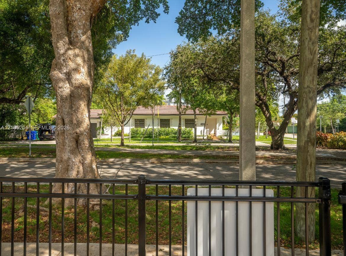 2121 SW 13th Avenue, #Studio, Miami, Miami, FL 33145 Single-story residence featuring a light-toned exterior, dark-toned hip roof, and mature trees situated on a parcel with metal perimeter fencing