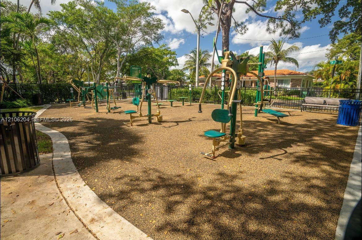 2121 SW 13th Avenue, #Studio, Miami, Miami, FL 33145 Outdoor fitness area featuring a rubberized surface, multiple static exercise stations, bench seating, and perimeter fencing shaded by mature trees