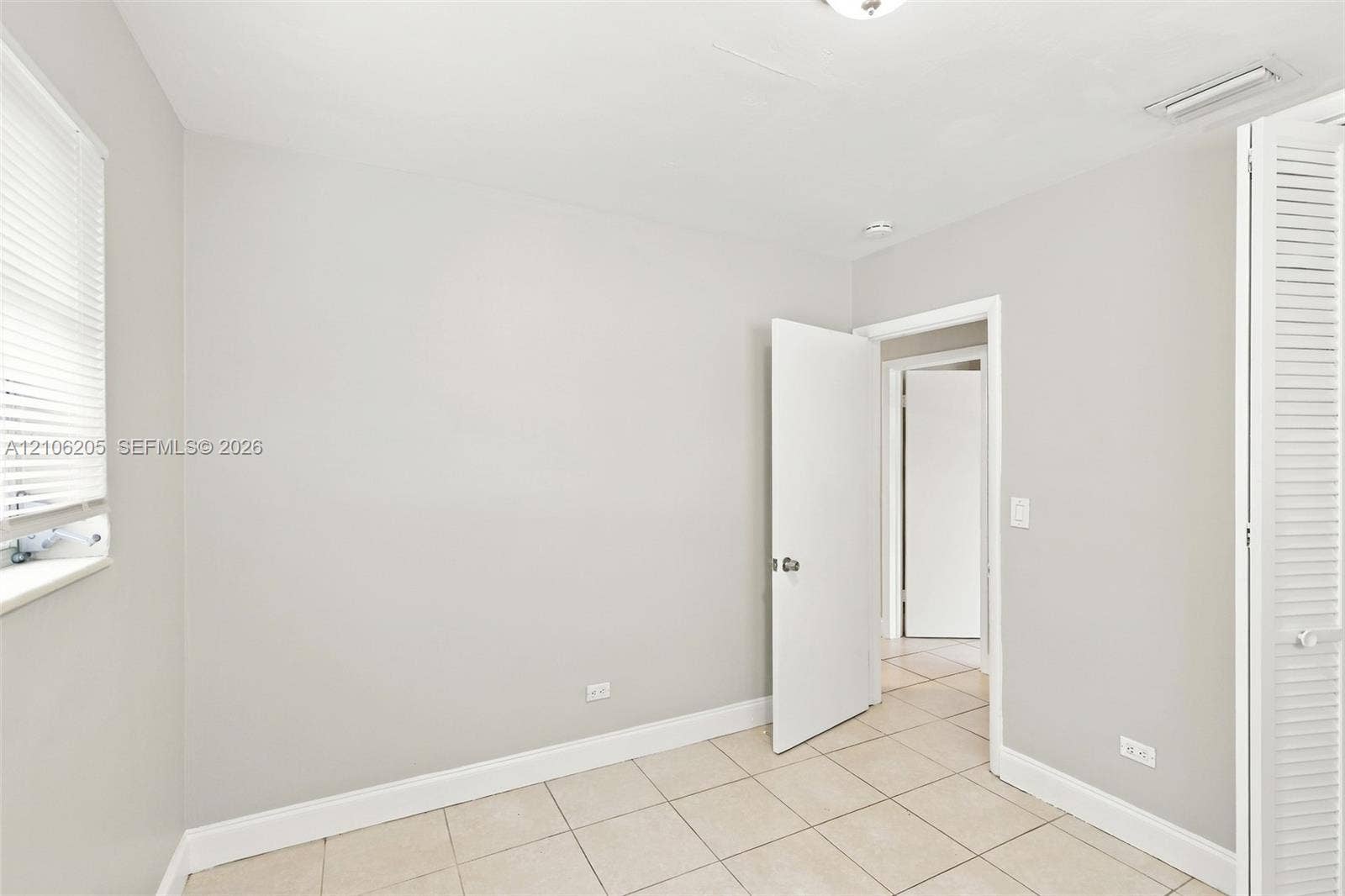 6941 SW 5th Street, Pembroke Pines, Pembroke Pines, FL 33023 Neutral-toned interior space featuring large-format tile flooring, a window with horizontal blinds, and louvered closet doors