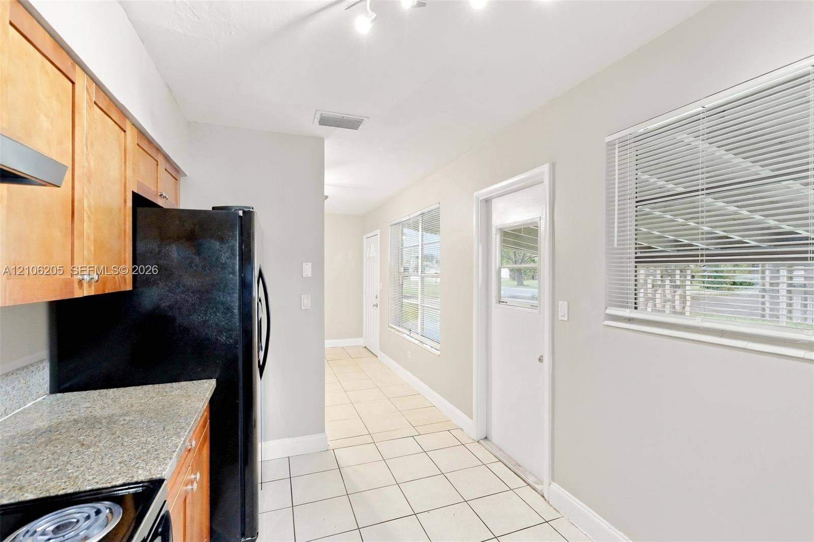 6941 SW 5th Street, Pembroke Pines, Pembroke Pines, FL 33023 Kitchen featuring natural finish wood cabinetry, stone-texture countertops, ceramic tile flooring, and multiple exterior-access doors
