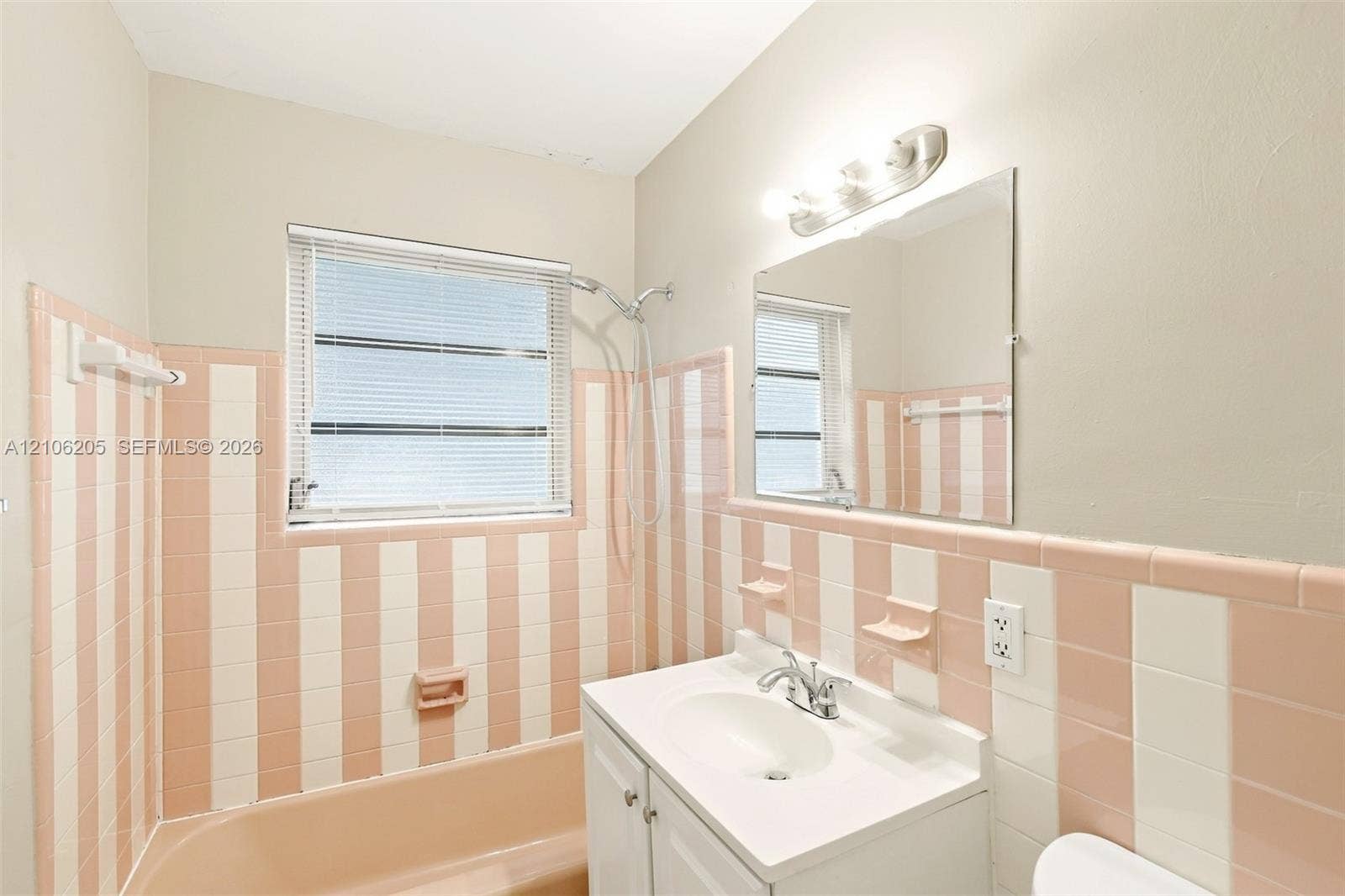 6941 SW 5th Street, Pembroke Pines, Pembroke Pines, FL 33023 Wall-mounted vanity with a porcelain sink and chrome faucet, rectangular wall mirror, three-light vanity fixture, and full-height striped ceramic wall tiling surrounding the porcelain bathtub