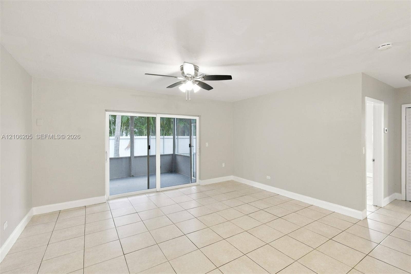 6941 SW 5th Street, Pembroke Pines, Pembroke Pines, FL 33023 Neutral-toned interior featuring ceramic tile flooring, a multi-blade ceiling fan with integrated lighting, and a sliding glass door providing external access to a screened enclosure