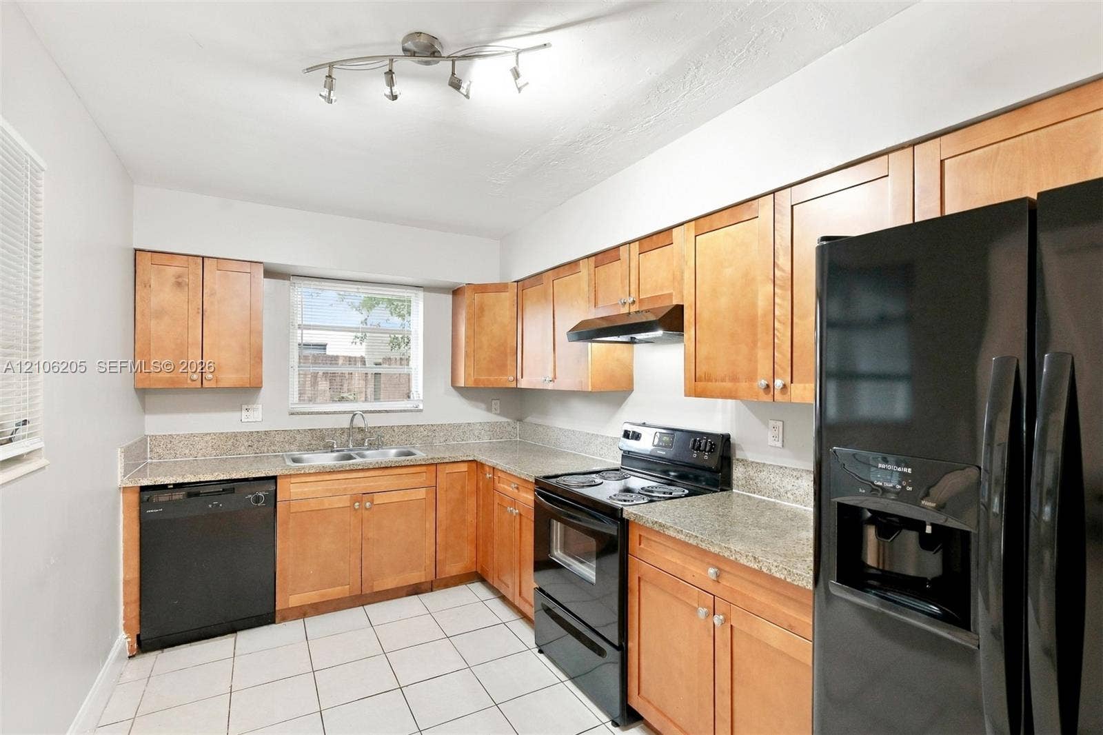 6941 SW 5th Street, Pembroke Pines, Pembroke Pines, FL 33023 Kitchen featuring wood cabinetry, stone-finish countertops, black appliances, a double-basin stainless steel sink, and tile flooring