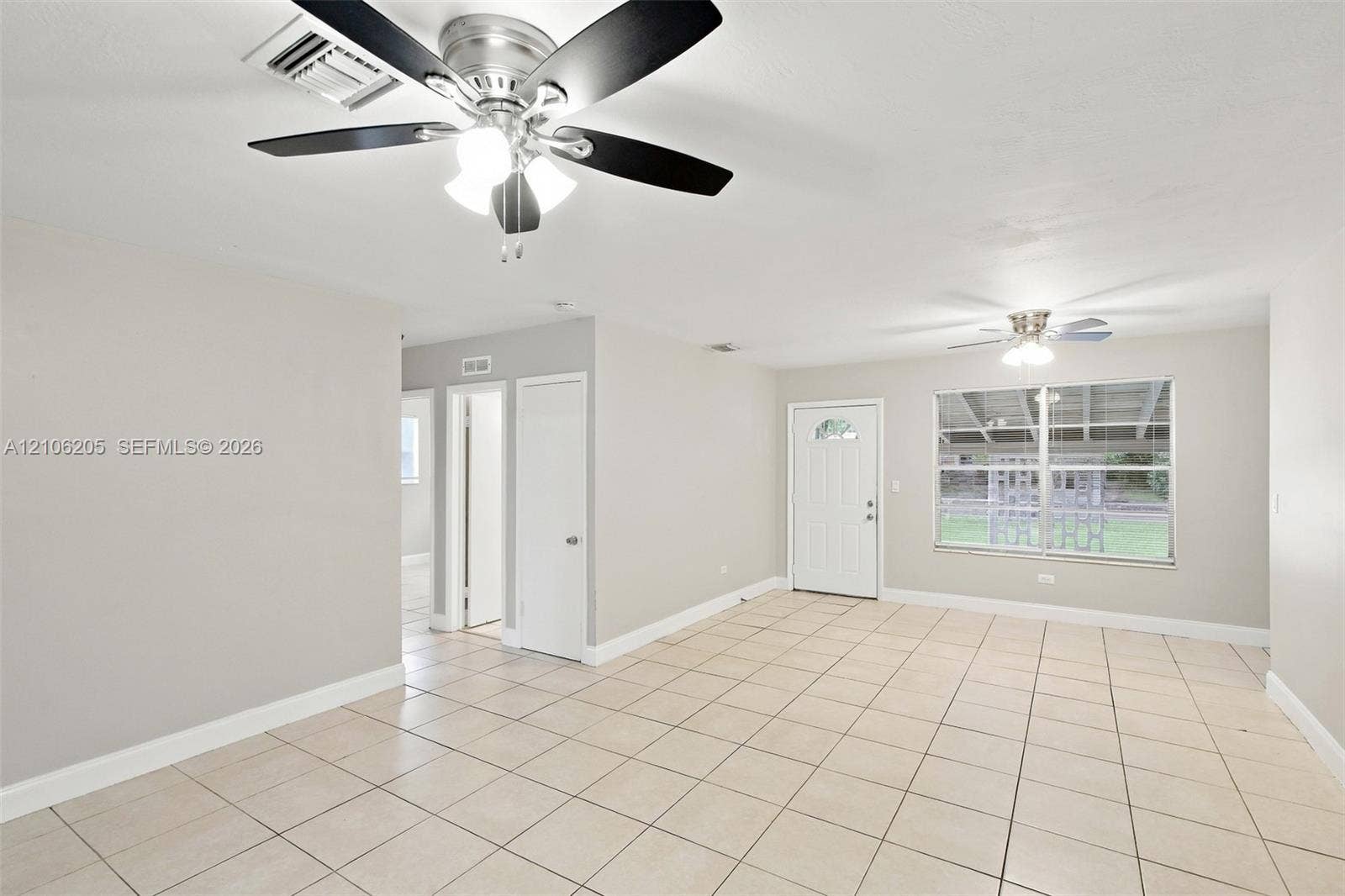 6941 SW 5th Street, Pembroke Pines, Pembroke Pines, FL 33023 Interior space featuring large-format neutral floor tile, dual ceiling fans with integrated lighting, a solid-core exterior door with a decorative glass insert, and a wide-pane window