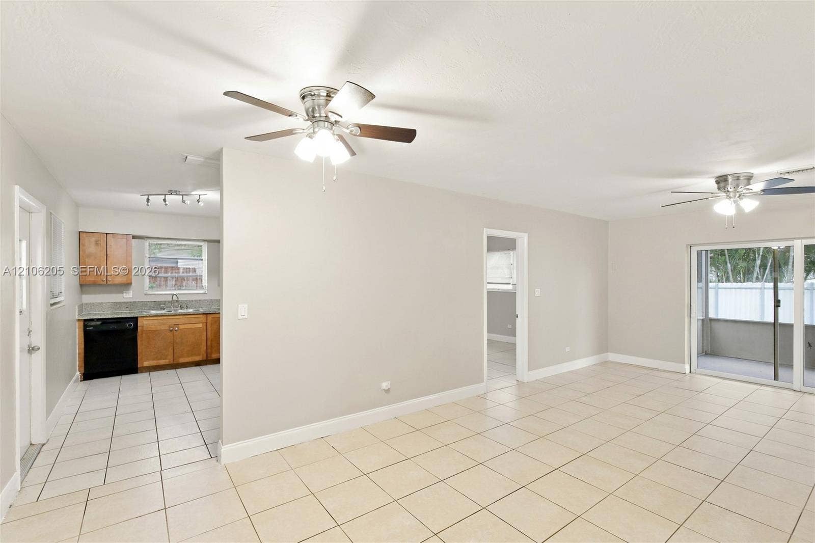 6941 SW 5th Street, Pembroke Pines, Pembroke Pines, FL 33023 Open-concept interior featuring light-toned tile flooring, dual ceiling fans, sliding glass doors, and a kitchen equipped with wood-finish cabinetry and stone-surface countertops