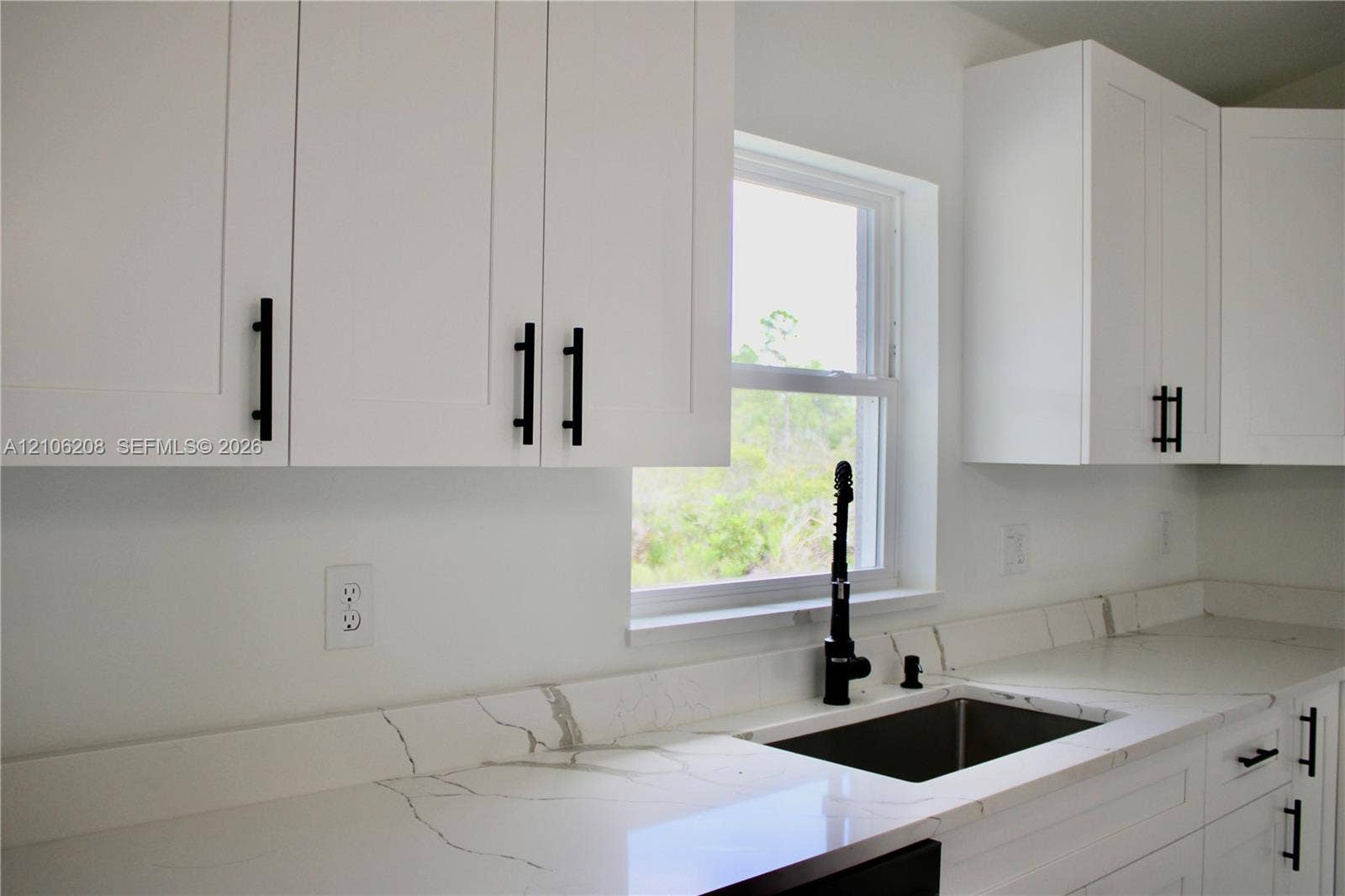 White shaker-style cabinetry with matte black pulls, light-toned stone-finish countertops with veining, under-mount stainless steel sink, and a matte black gooseneck faucet