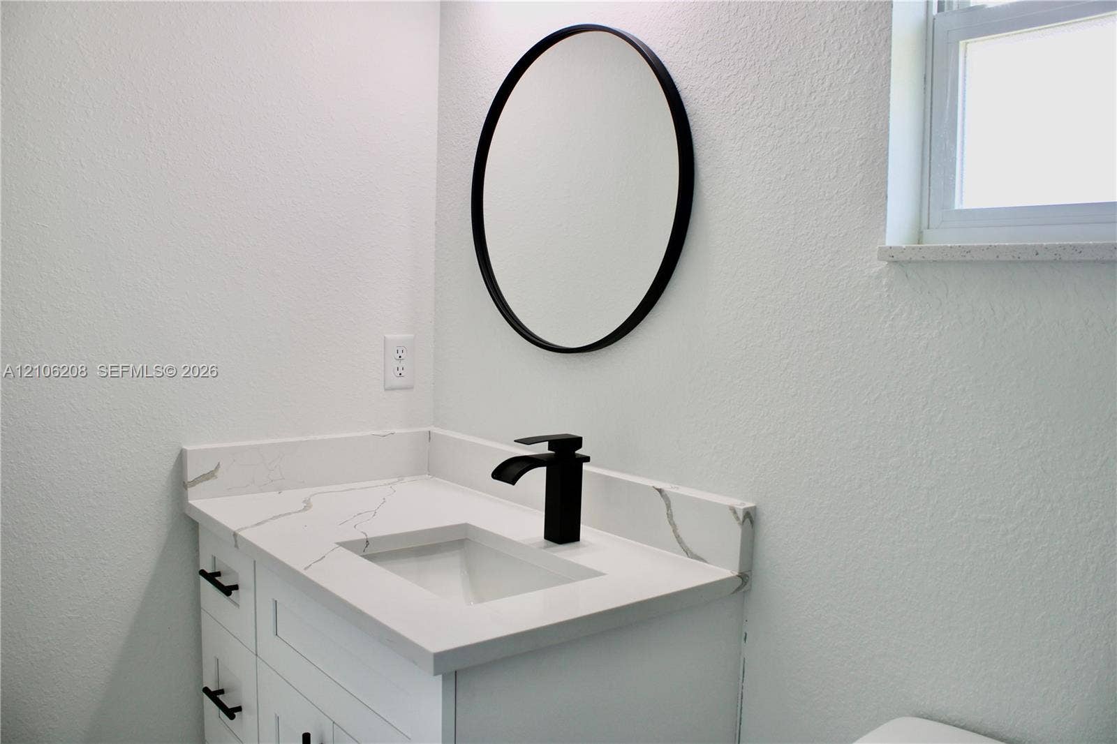 White vanity featuring a stone-look countertop, integrated rectangular sink, matte black faucet, and circular wall-mounted mirror