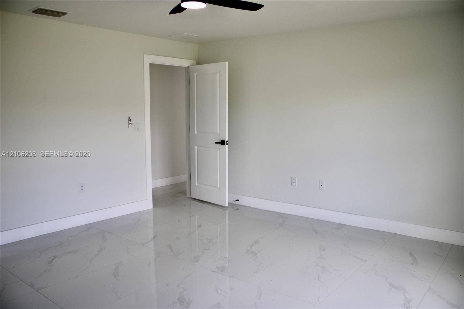 Interior room featuring light-toned, large-format tile flooring with a subtle veined pattern, a two-panel interior door with matte black hardware, and a ceiling-mounted matte black fan