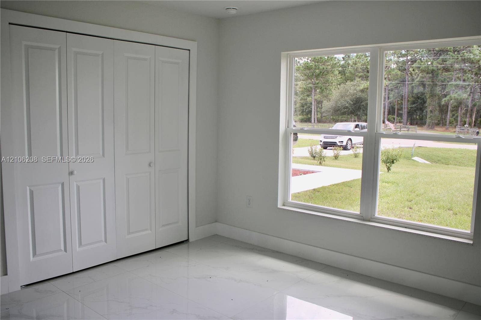 Room with polished tile flooring, white interior finishes, multi-panel closet doors, and large dual-pane windows