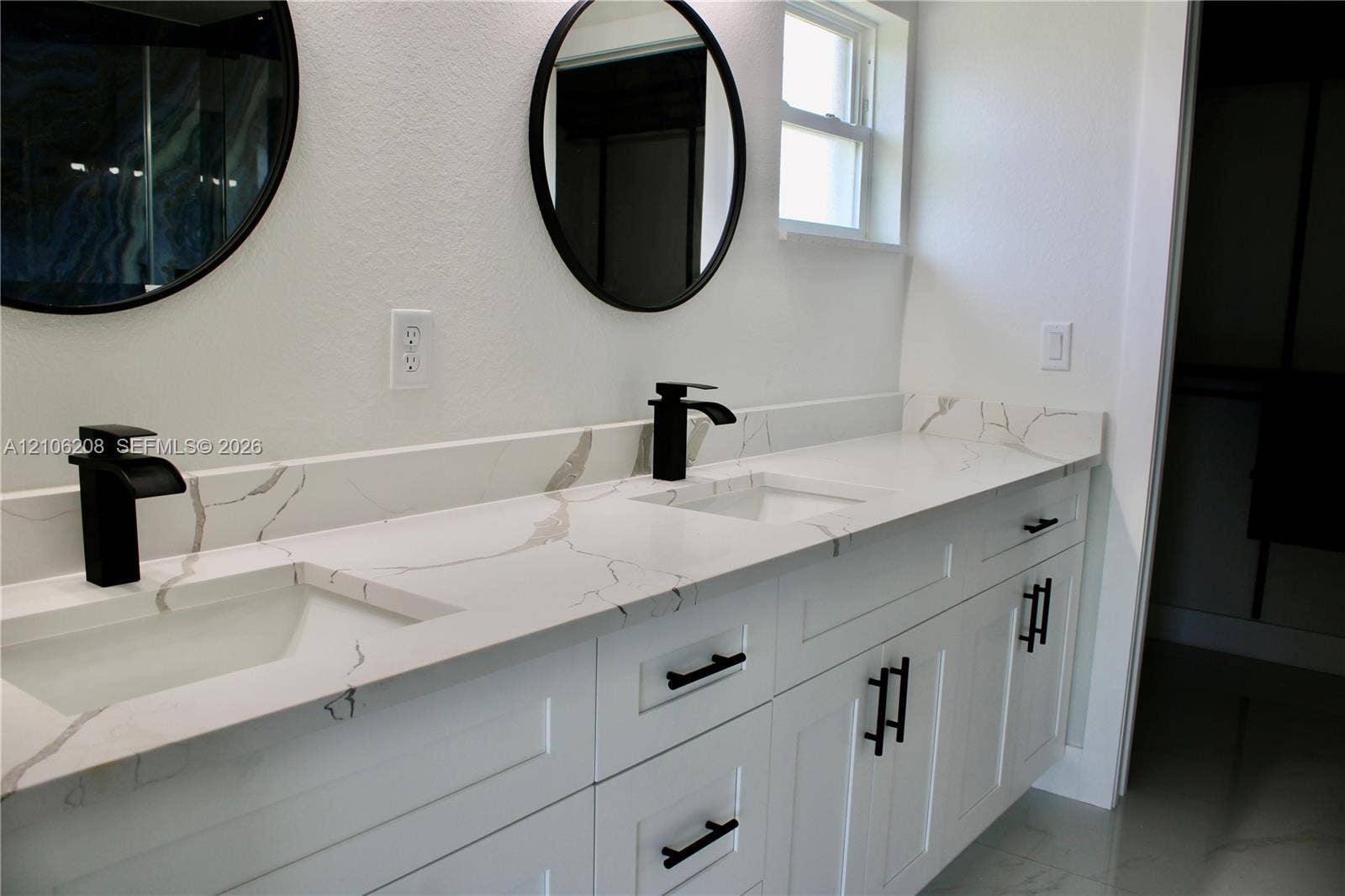 Dual-vanity cabinet featuring white shaker-style doors, matte black hardware, stone-patterned countertops, undermount sinks, and circular wall-mounted mirrors with matte black frames