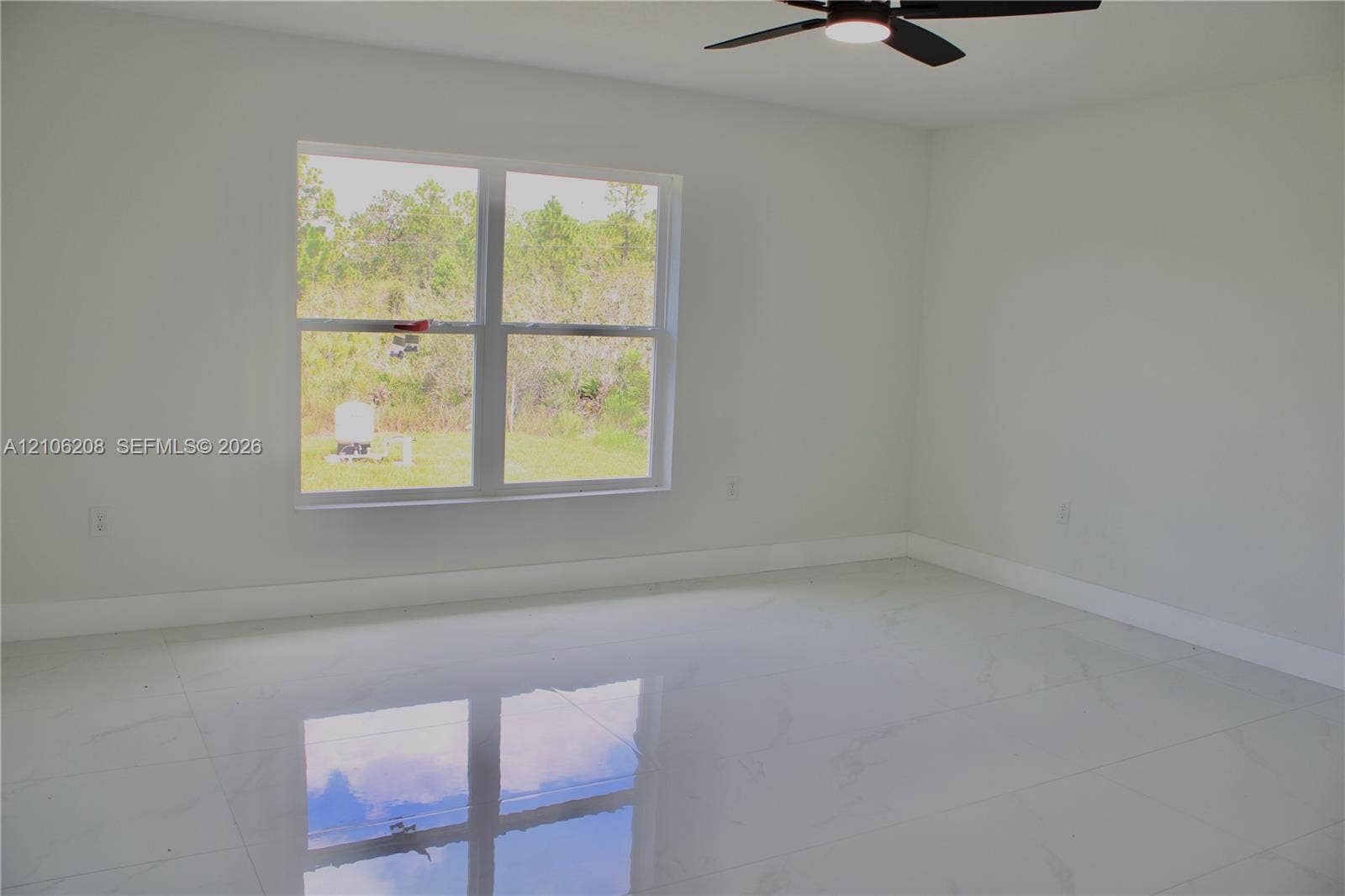 Spacious interior featuring large-format tile flooring, neutral wall tones, a ceiling fan with integrated lighting, and a multi-pane window