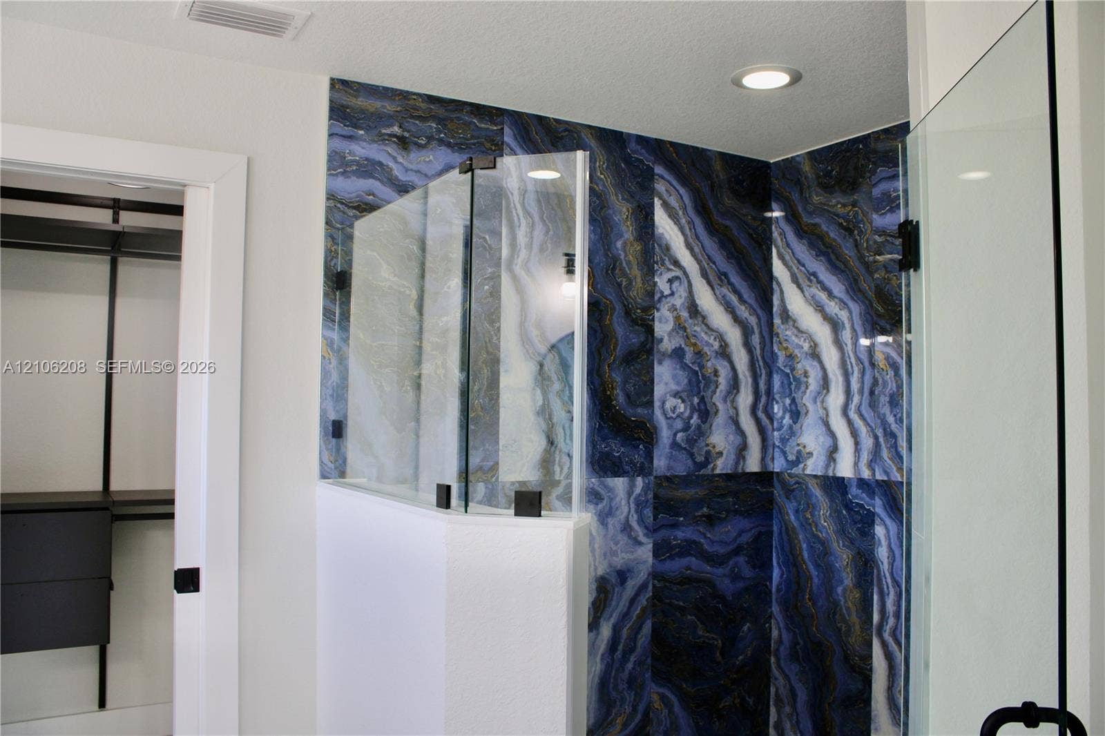 Walk-in shower featuring large-format blue and gold decorative wall tile, frameless glass enclosure, matte black hardware, and recessed ceiling lighting