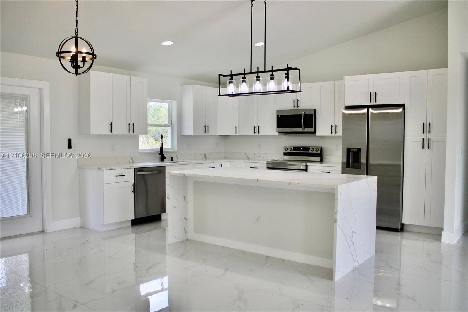 Kitchen featuring white shaker-style cabinetry, an expansive waterfall-edge island with stone-finish countertops, stainless steel appliances, polished stone-finish flooring, and linear multi-bulb pendant lighting