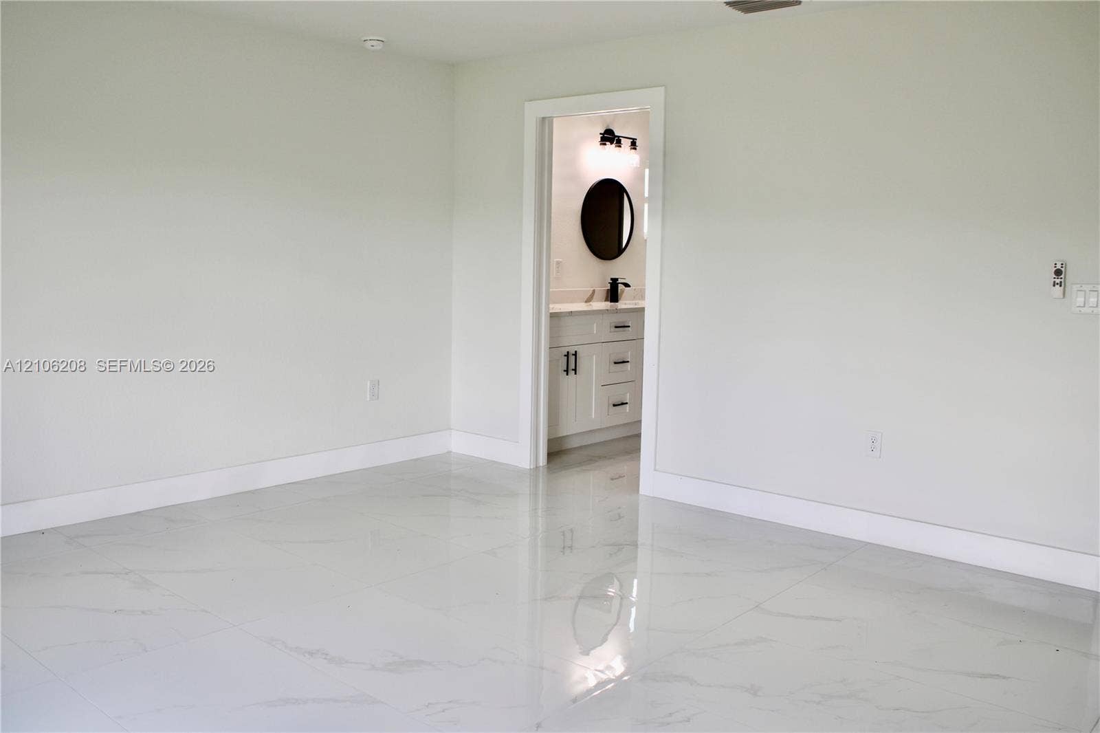 Large-format tile flooring with a stone-finish pattern, paired with a vanity featuring a light-toned countertop, undermount sink, circular wall mirror, and matte black hardware