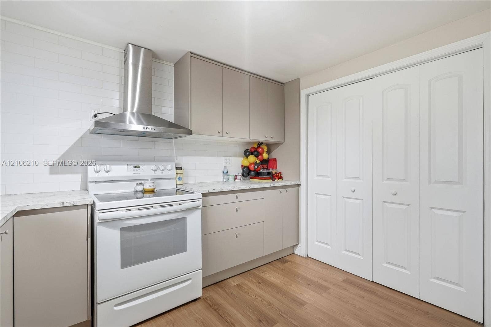 1111 S 7th Street, Fort Pierce, FL 34950 Kitchen featuring flat-panel cabinetry, stone-finish countertops, white subway tile backsplash, stainless steel chimney-style range hood, and wood-finish flooring