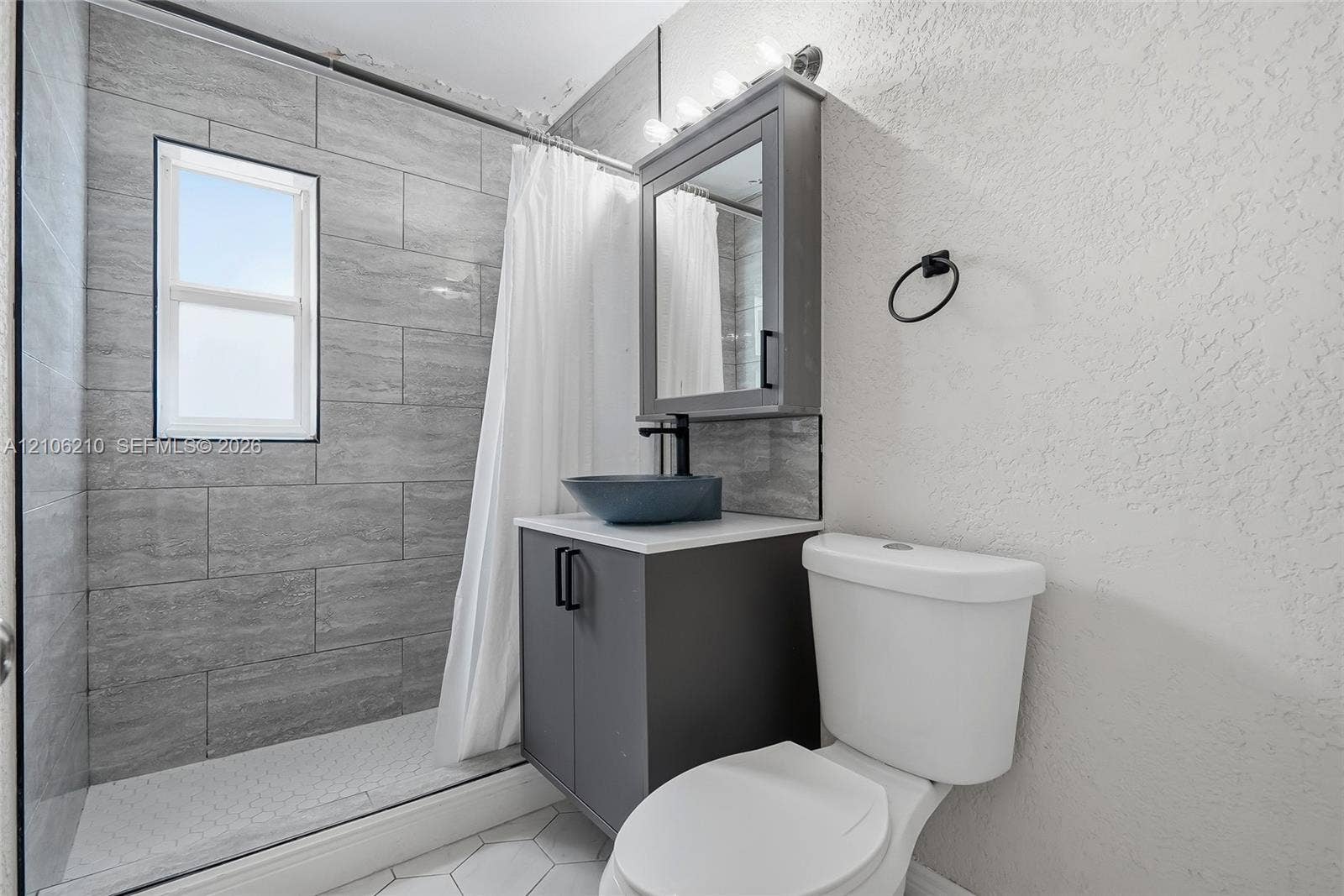 1111 S 7th Street, Fort Pierce, FL 34950 Bathroom featuring a walk-in shower with grey horizontal tile surround, grey vanity cabinet, vessel sink, and mirrored medicine cabinet