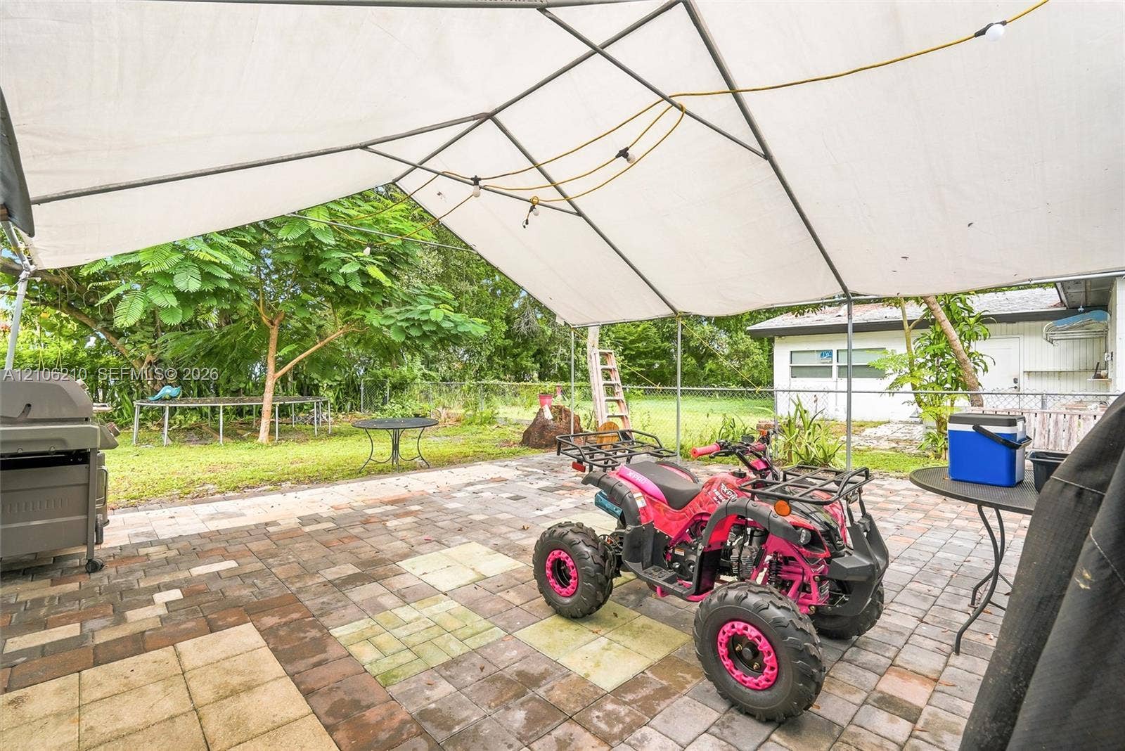 1111 S 7th Street, Fort Pierce, FL 34950 Paver patio area featuring a metal-framed canopy structure, chain-link perimeter fencing, and mature trees