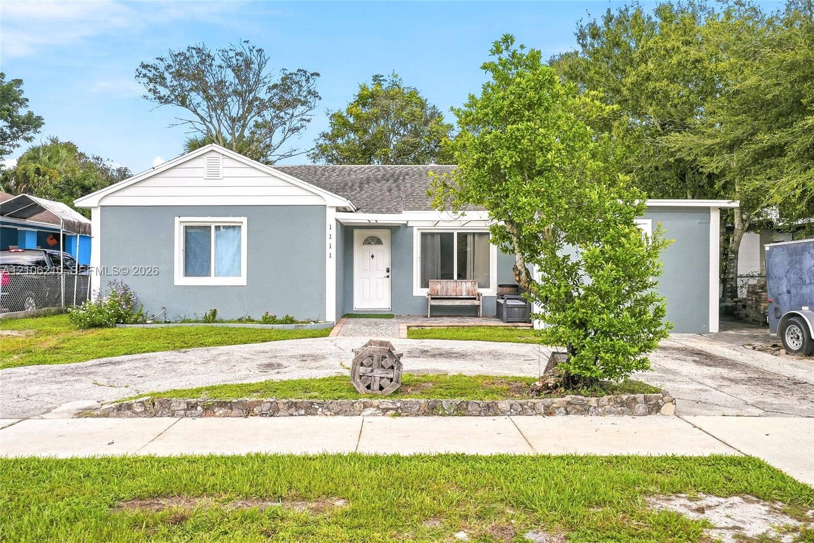 1111 S 7th Street, Fort Pierce, FL 34950 Single-story exterior featuring a grey smooth-finish facade, white horizontal gable siding, a pitched asphalt shingle roof, and a paved stone walkway