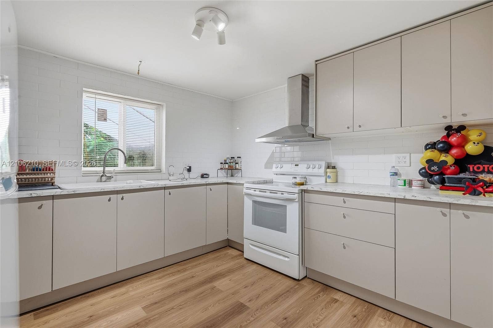 1111 S 7th Street, Fort Pierce, FL 34950 Kitchen featuring flat-panel cabinetry, stone-finish countertops, subway tile backsplash, stainless steel range hood, and wood-finish flooring