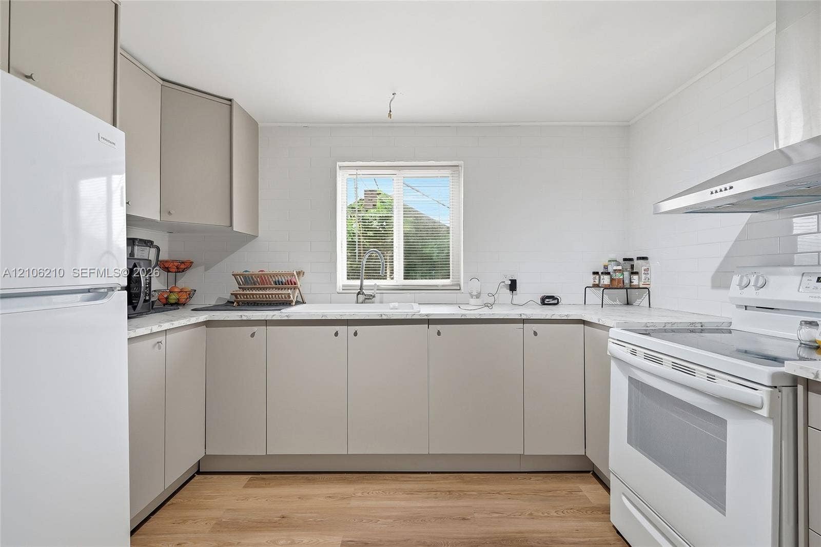 1111 S 7th Street, Fort Pierce, FL 34950 Kitchen featuring light gray flat-panel cabinetry, white solid surface countertops, a stainless steel range hood, and wood-finish flooring