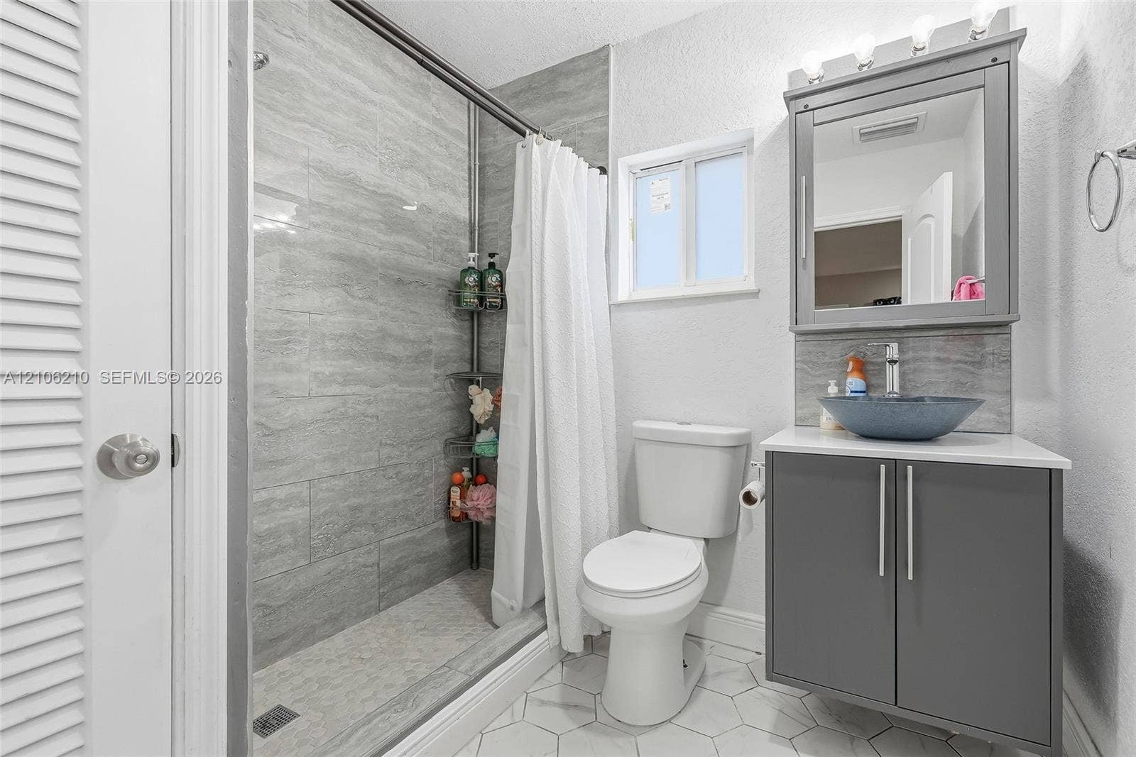1111 S 7th Street, Fort Pierce, FL 34950 Bathroom featuring a shower stall with stone-finish tile surround, vanity with a vessel sink, integrated medicine cabinet, and white hexagonal floor tile