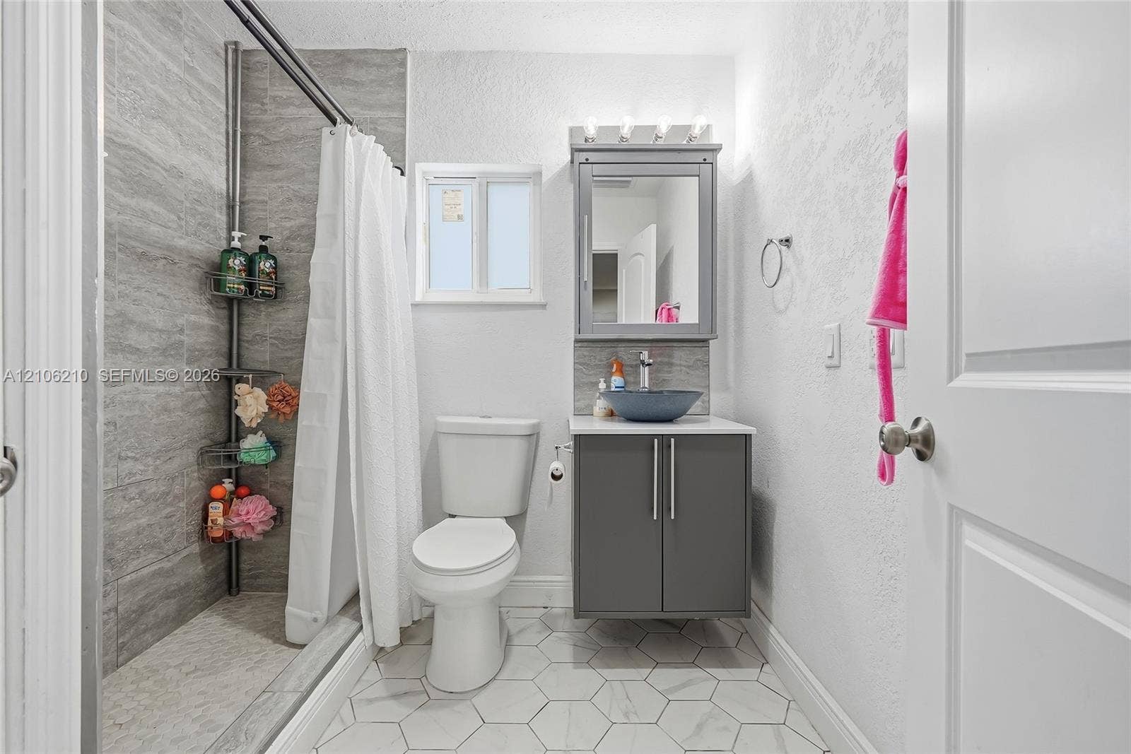 1111 S 7th Street, Fort Pierce, FL 34950 Bathroom featuring a walk-in shower with grey horizontal tile surround, grey vanity cabinet, stone-finish countertop with a vessel sink, and white hexagonal floor tile