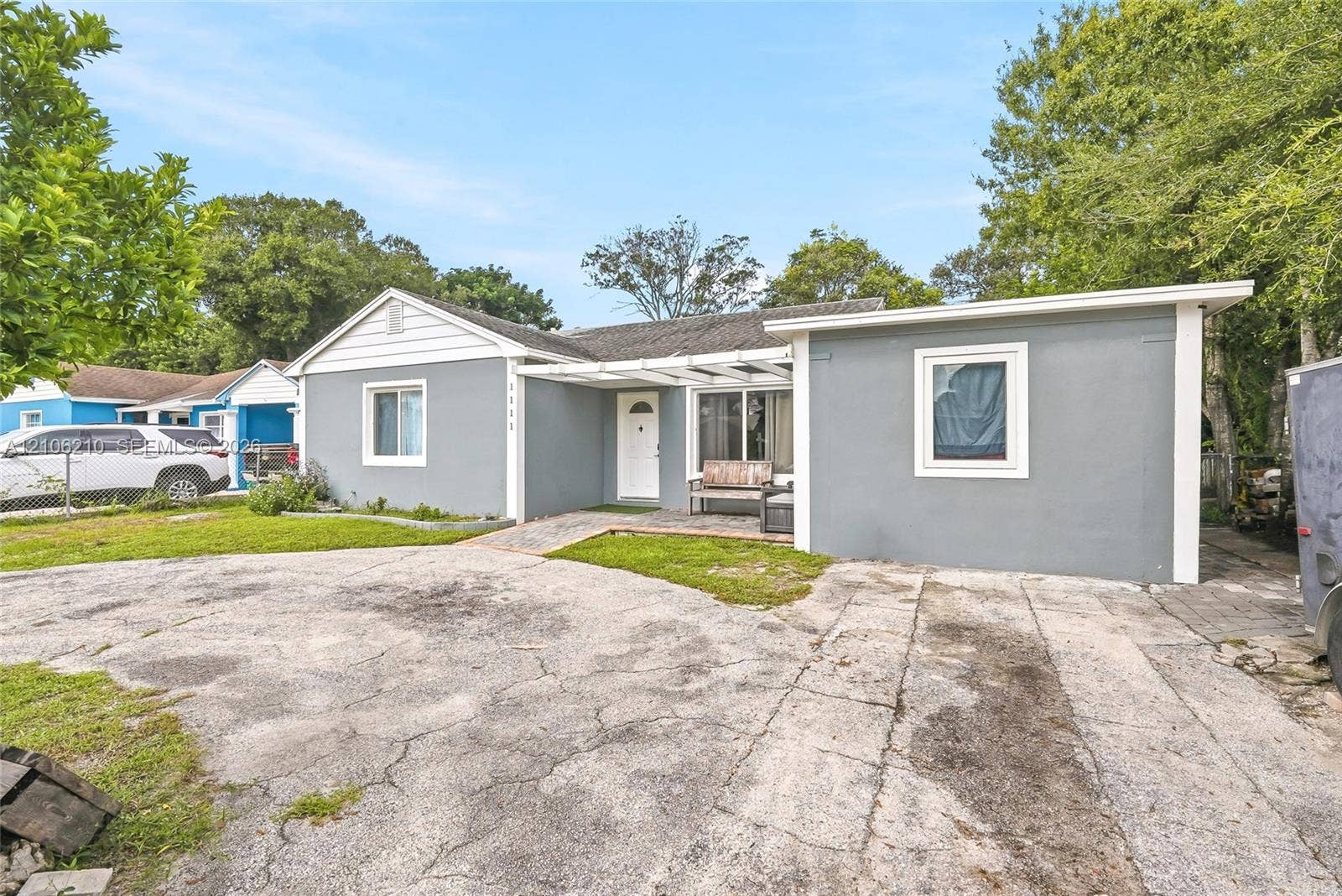 1111 S 7th Street, Fort Pierce, FL 34950 Exterior facade featuring gray painted masonry, a white-trimmed gabled roofline, a paved driveway, and an open-frame covered entryway