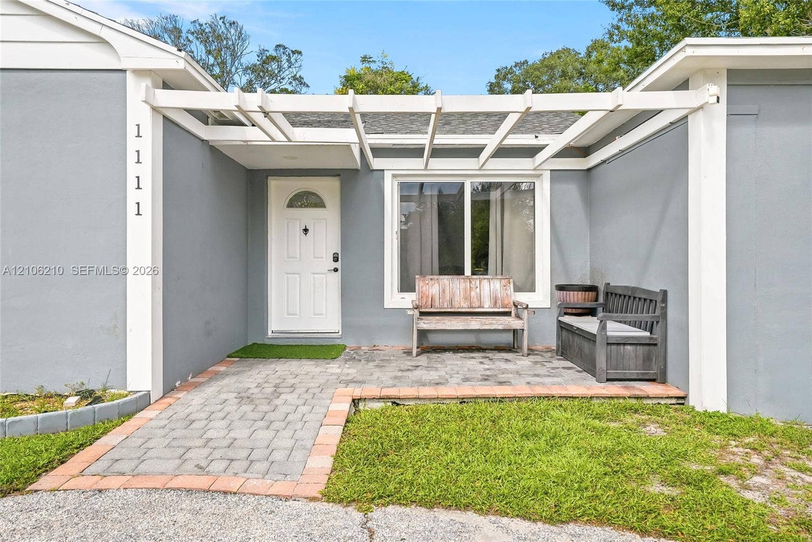 1111 S 7th Street, Fort Pierce, FL 34950 Exterior entryway featuring a white pergola, paver patio, brick edging, and a single-light panel front door