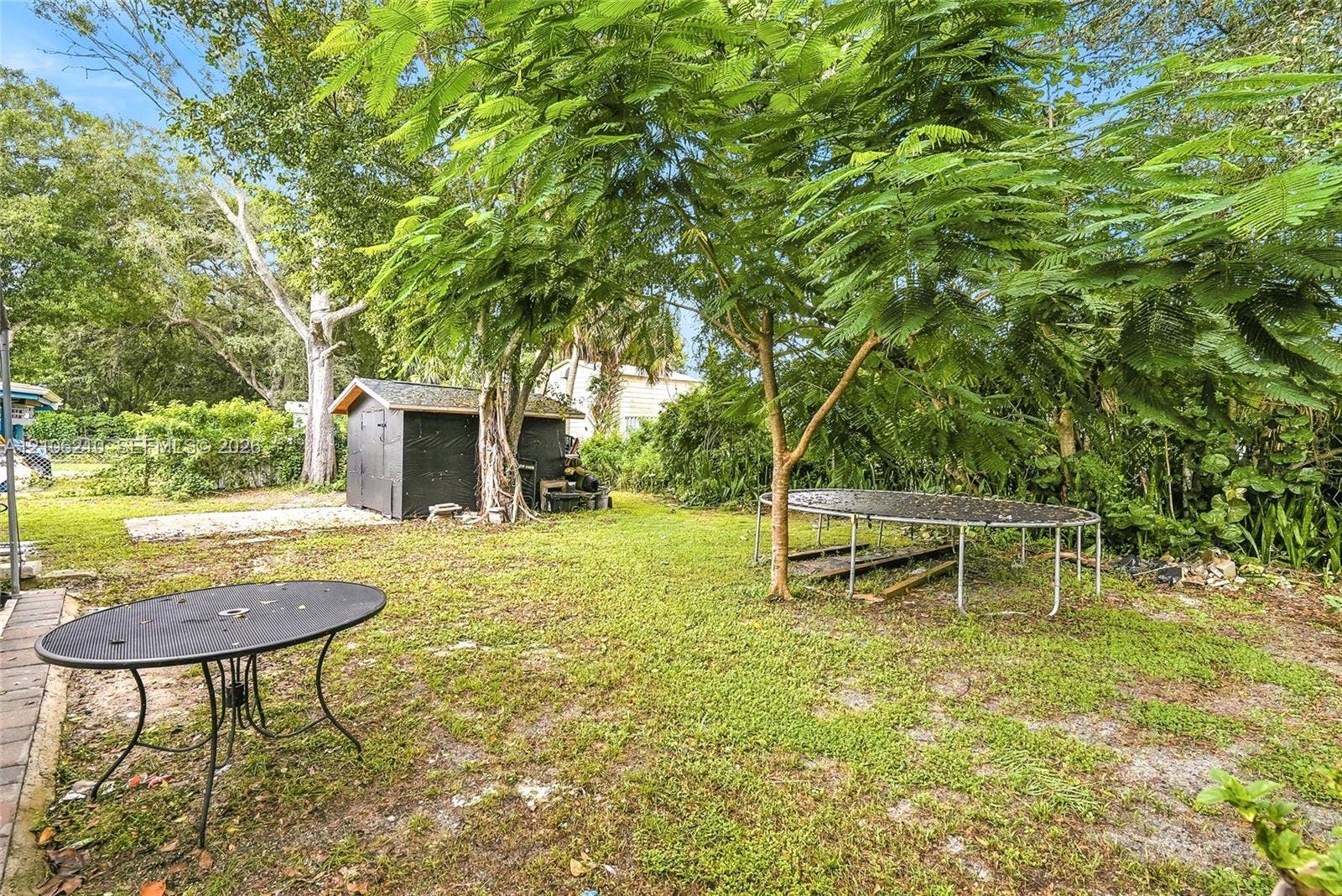 1111 S 7th Street, Fort Pierce, FL 34950 Expansive backyard featuring mature shade trees, a detached storage structure, and a graveled ground cover area