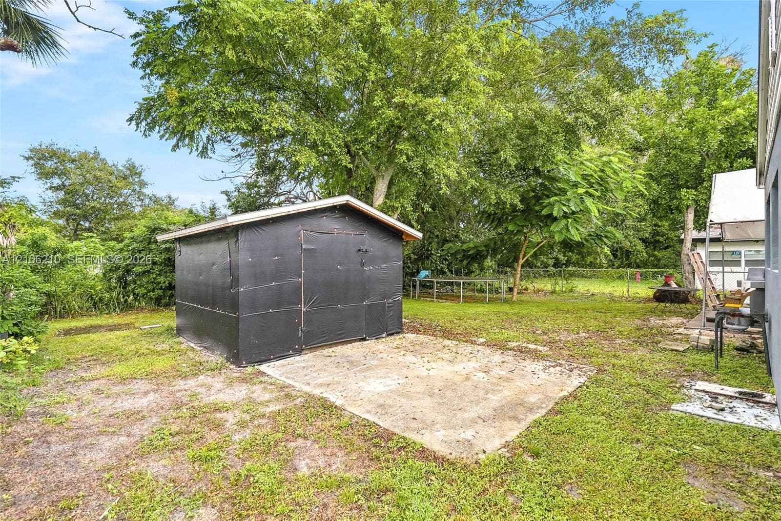 1111 S 7th Street, Fort Pierce, FL 34950 Backyard area featuring a structural storage shed, concrete foundation pad, chain-link fencing, and mature trees