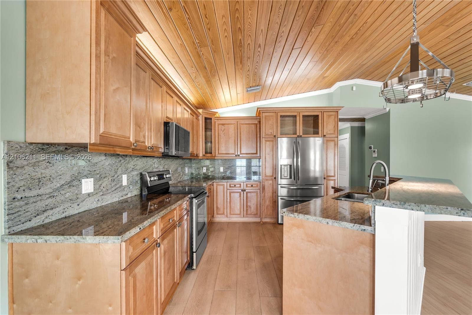 Kitchen featuring natural wood-finish cabinetry, stone slab countertops, stainless steel appliances, vaulted wood-paneled ceiling, and a hanging metal light fixture