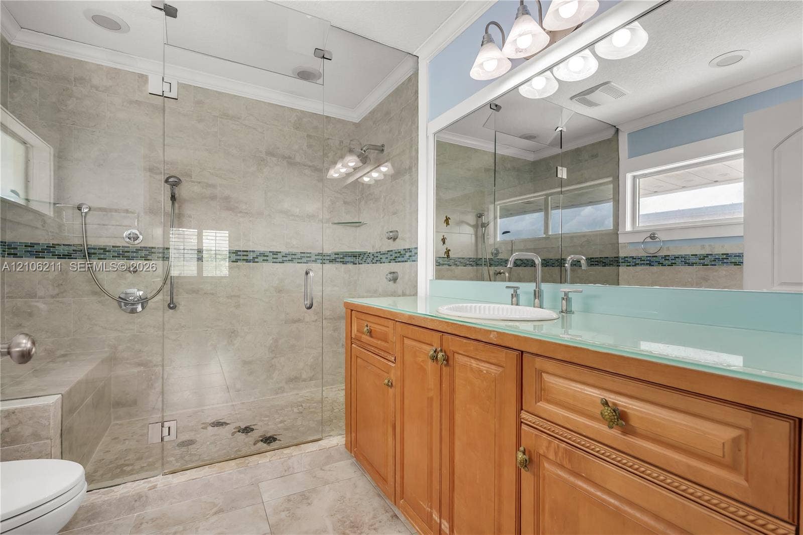 Walk-in shower with floor-to-ceiling tile, integrated seating, glass enclosure, and multi-head shower system; vanity featuring light-toned cabinetry and a solid-surface countertop with an integrated sink