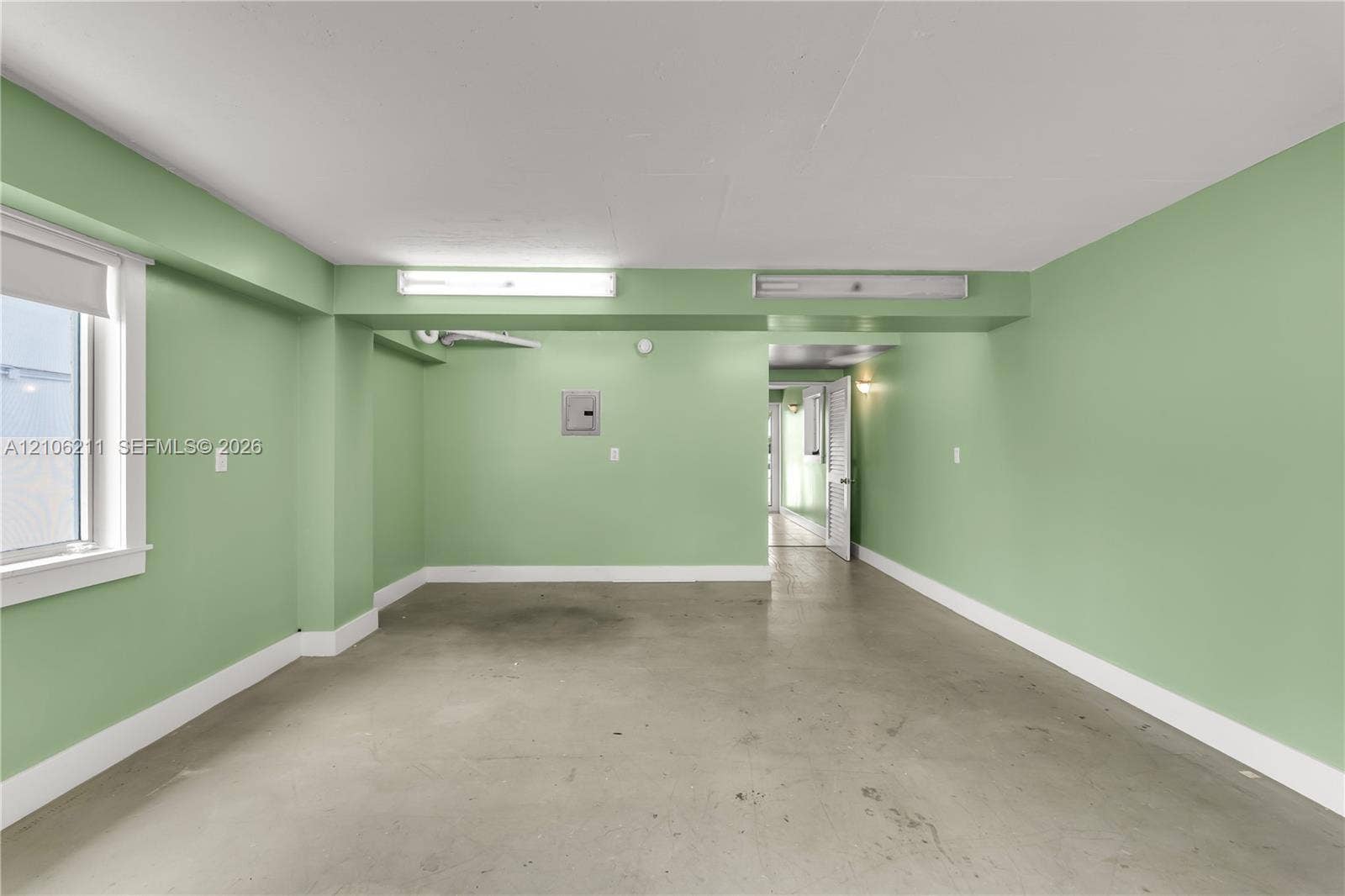 Multi-purpose interior space featuring smooth concrete flooring, overhead fluorescent lighting, and a single-pane window