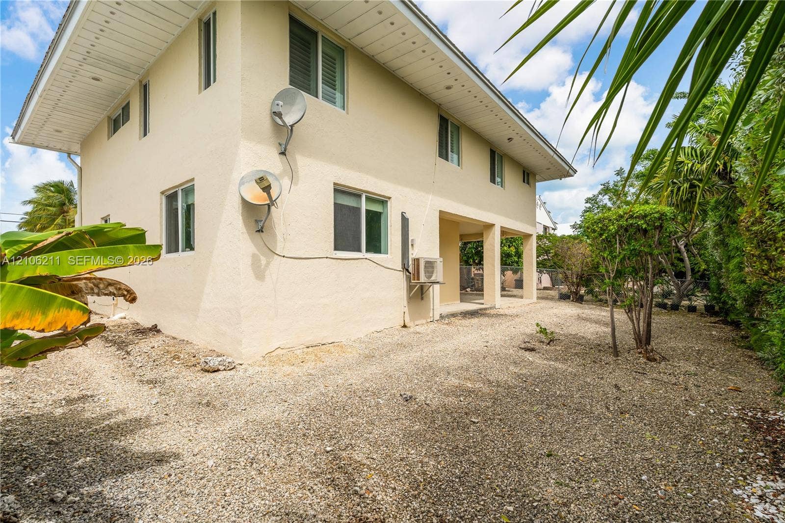 Stucco exterior featuring an expansive covered patio, multi-level structural design, wide roof overhangs, and a gravel-surfaced yard