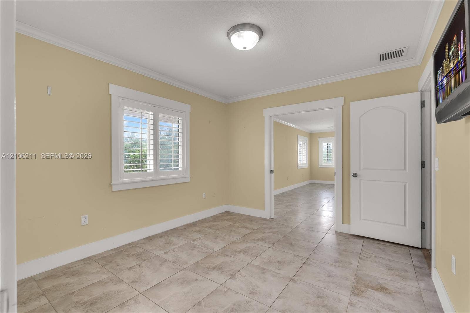 Neutral-toned interior featuring tile flooring, crown molding, arched two-panel interior door, and window shutters
