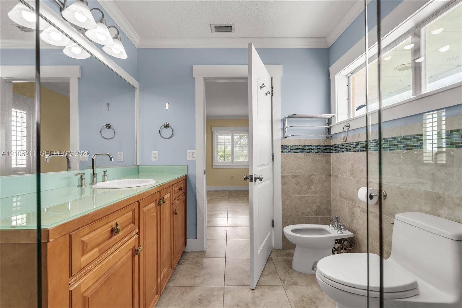 Bathroom featuring a wood vanity with a glass countertop, integrated sink, stone tile flooring, wall-mounted bidet, and mosaic tile accent border