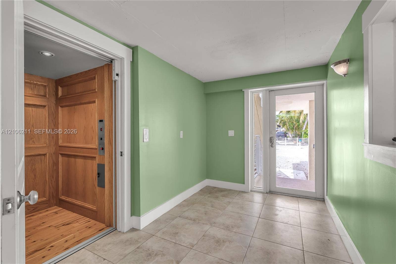 Interior elevator with wood-paneled walls and flooring, ceramic tile flooring, and glass-paned exterior door
