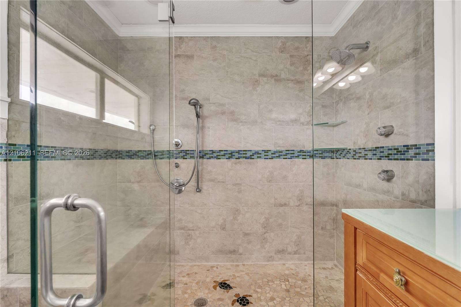 Walk-in shower featuring glass paneling, floor-to-ceiling tile with a decorative mosaic accent band, a built-in tiled bench, stone pebble flooring with inlaid tile motifs, and a multi-function shower system