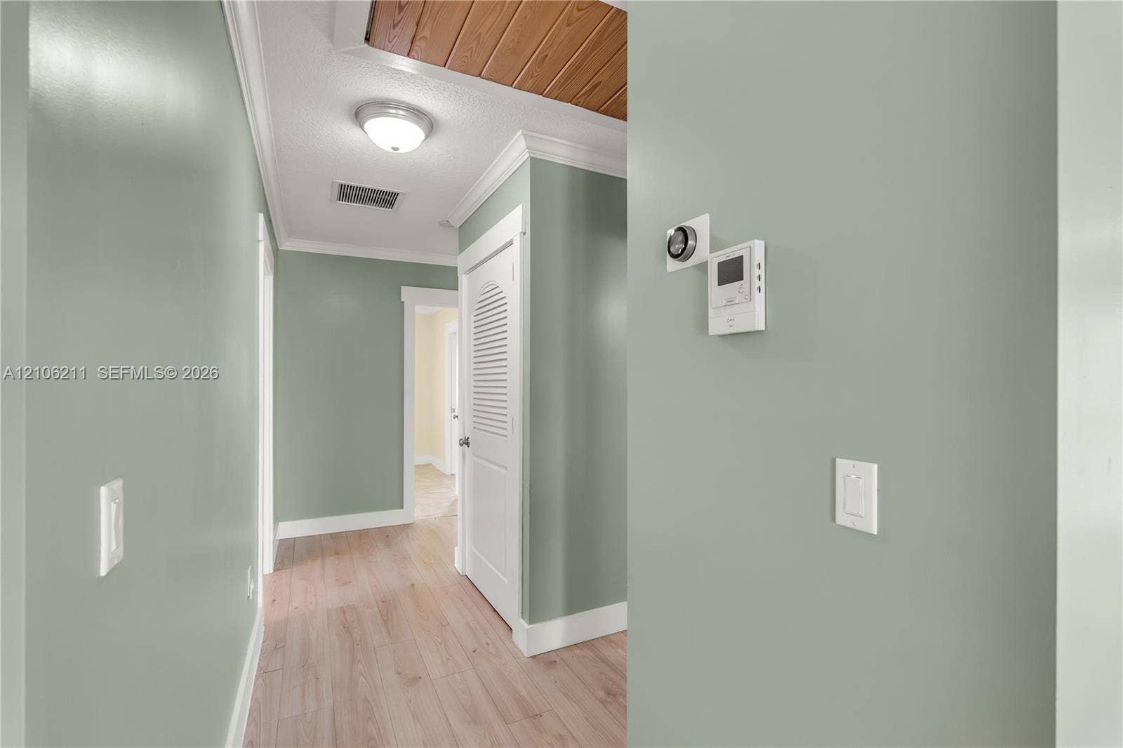 Hallway featuring wood-finish flooring, wood-paneled ceiling accent, crown molding, and a louvered-panel closet door