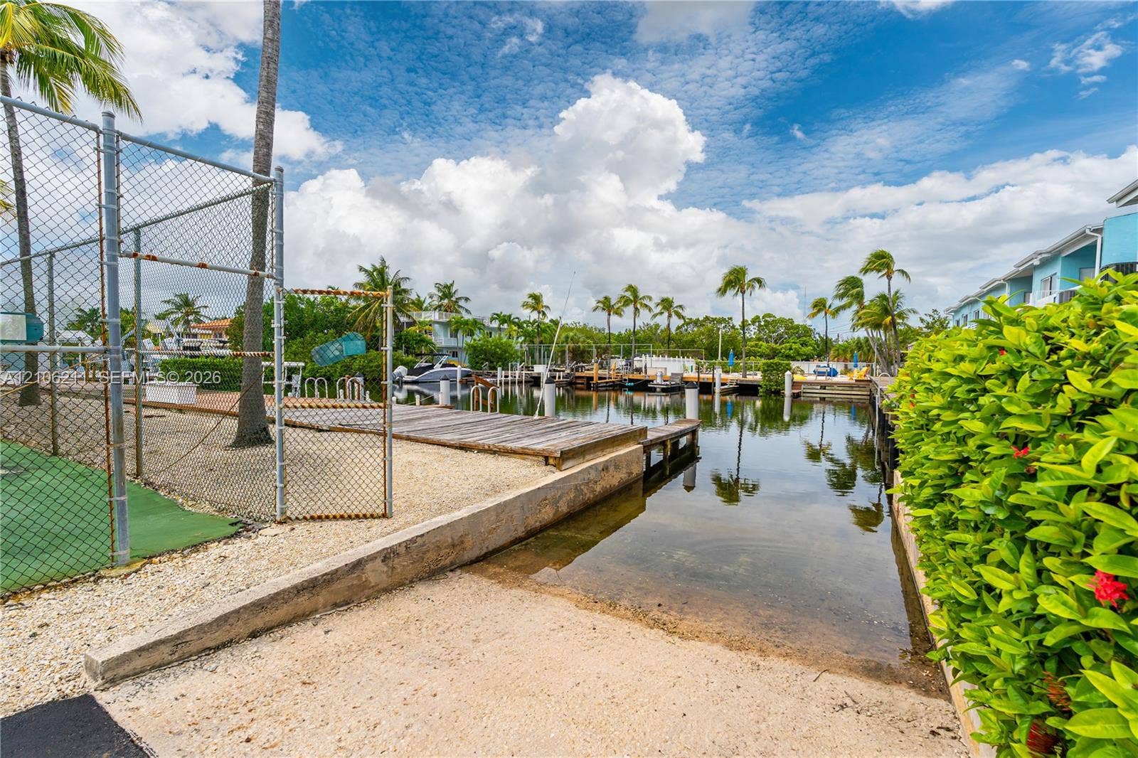 Waterfront boat slip with wooden decking, concrete retaining wall, and fenced recreational court area